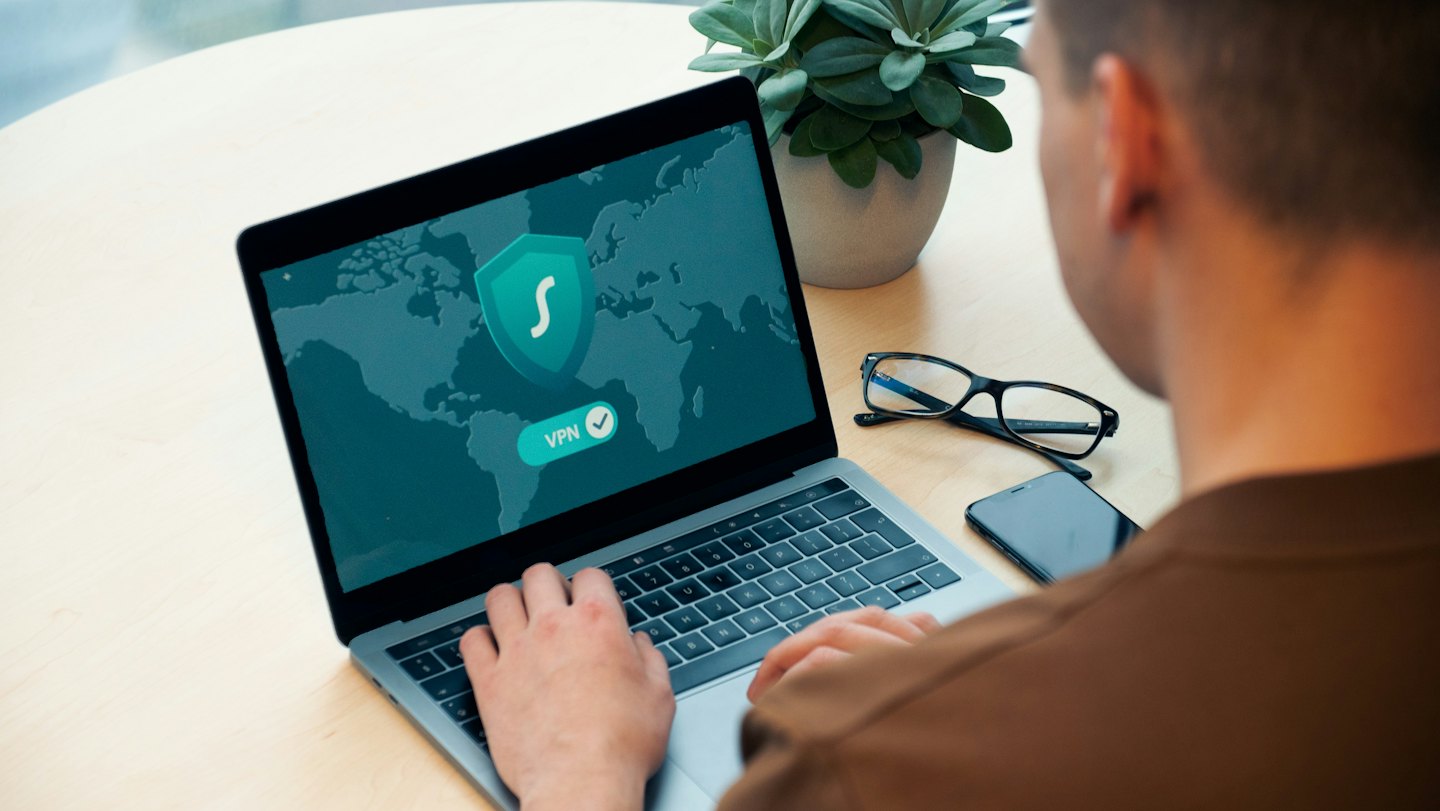 Person nutzt Laptop mit VPN-Verbindung auf einem Holztisch.