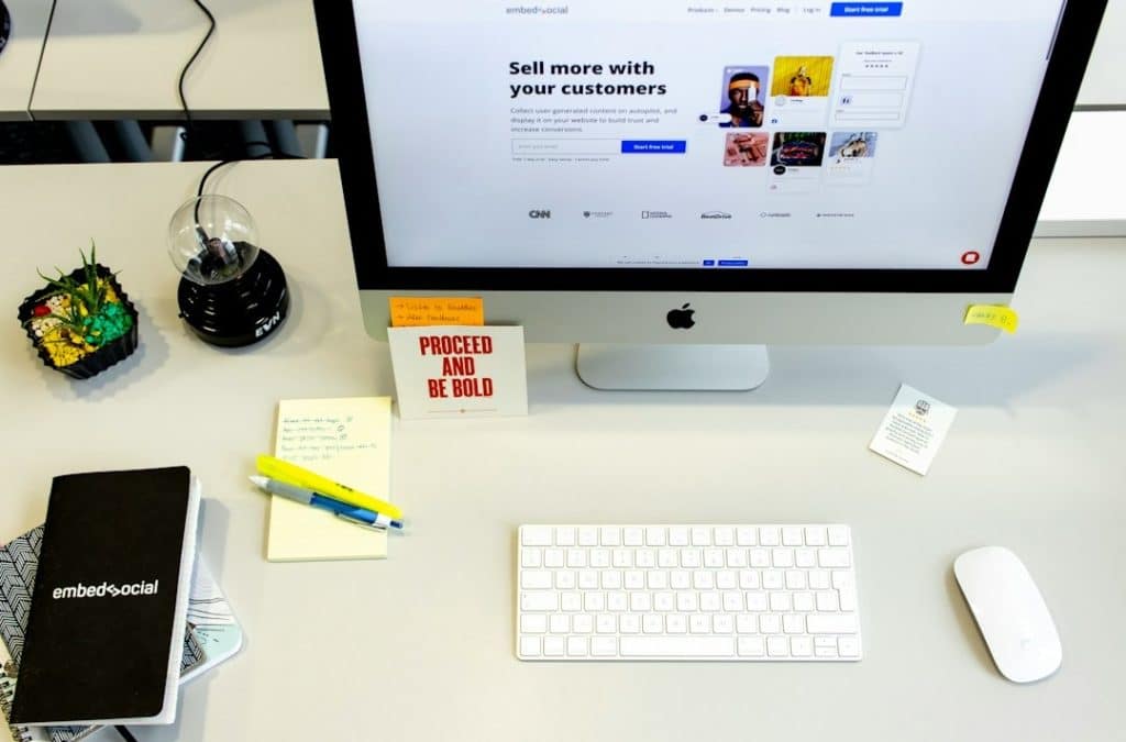 Modern office desk with iMac displaying 'embed>social' website.